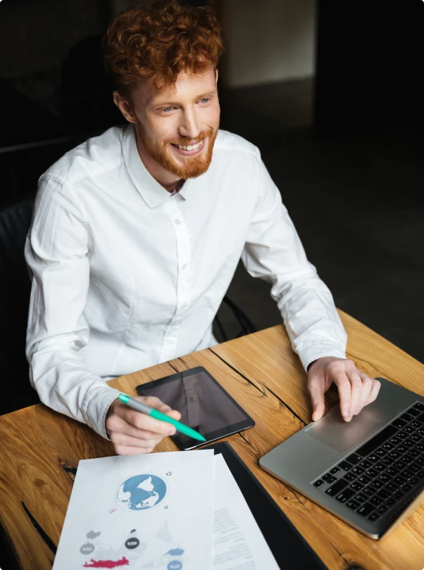 Smiling man working on a laptop and tablet at a desk