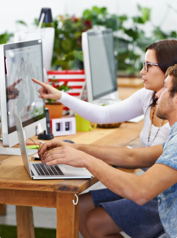 Colleague pointing at a monitor while a teammate types on a laptop
