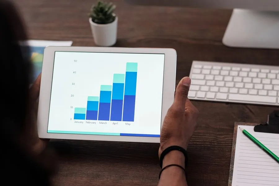 Hands holding a tablet that shows a stacked bar chart of monthly results
