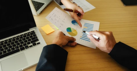 Hands marking up printed charts beside a laptop