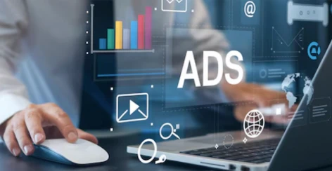 A hand on a mouse beside a laptop under an ads graphic overlay