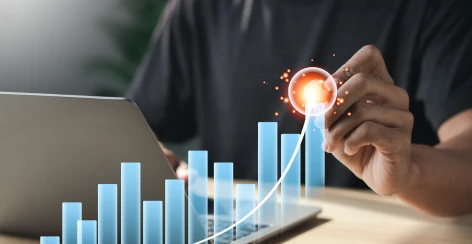Hand tracing a rising bar chart above a laptop