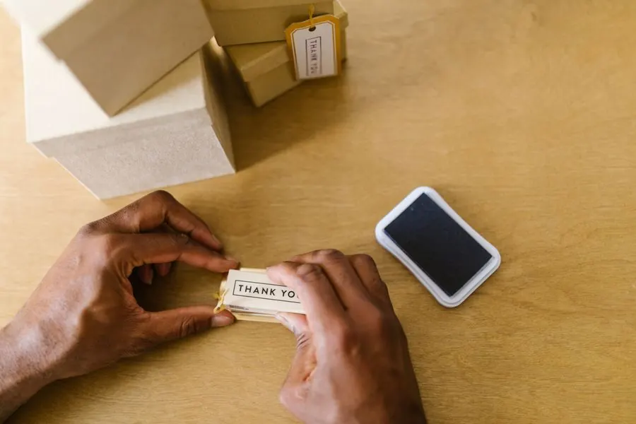 Hands stamping a thank-you tag beside boxed customer orders