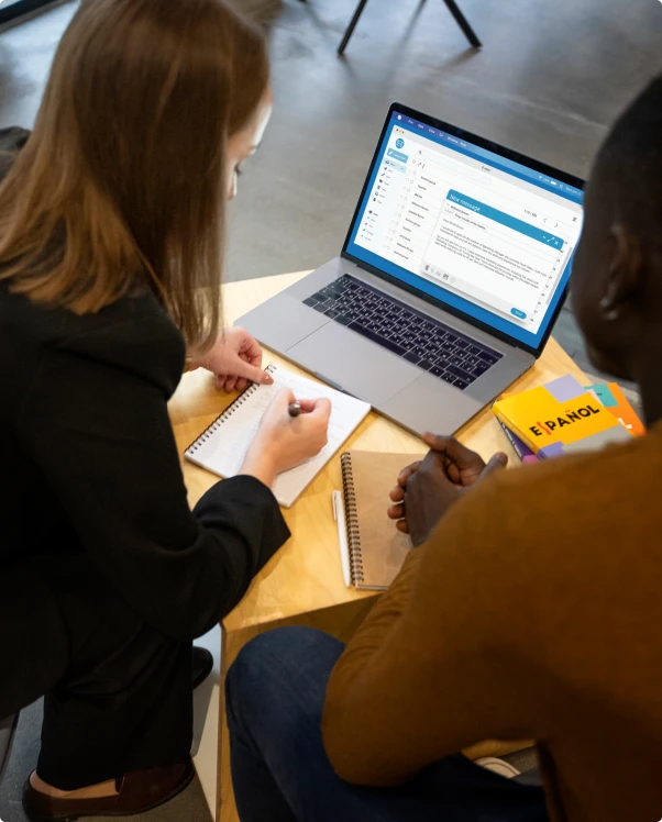 Two colleagues taking notes beside a laptop showing an email draft
