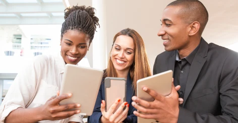 Three people smiling as they browse on tablets and a phone