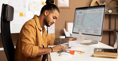 Designer sketching a landing page wireframe at a desktop monitor