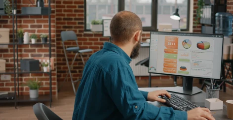 Man working at a monitor showing report charts in a brick-walled office